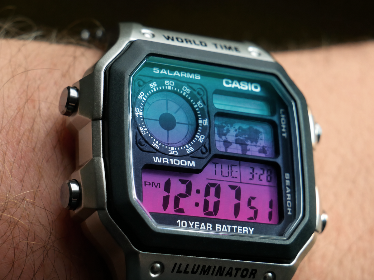 Close-up wrist view of the Aurora Gradient Casio AE-1200 showing the teal to violet to magenta gradient display