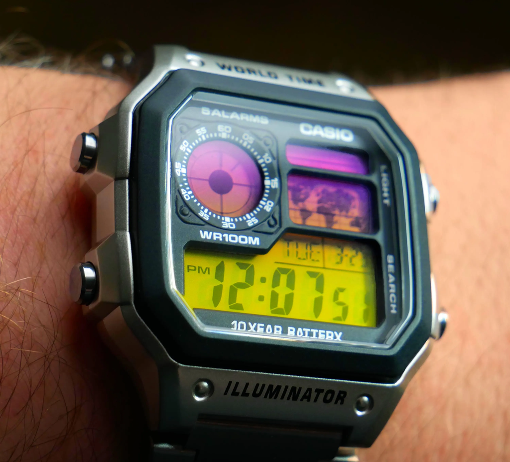 Close-up wrist view of a custom Casio AE-1200 with sunset-gradient display and stainless steel bracelet