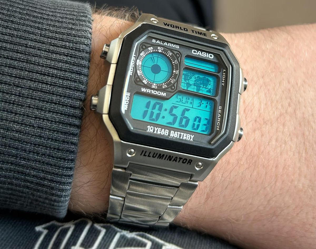Close-up wrist view of a custom Casio AE-1200 with turquoise-blue display and steel bracelet