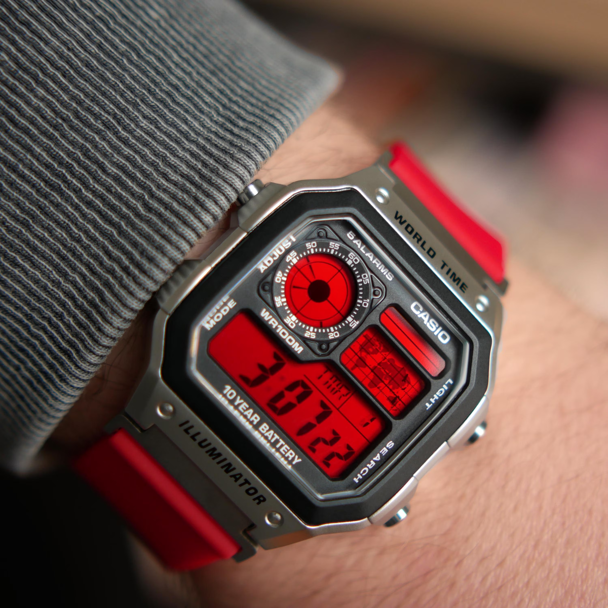 Close-up wrist view of a custom Casio AE-1200 with red display and resin strap